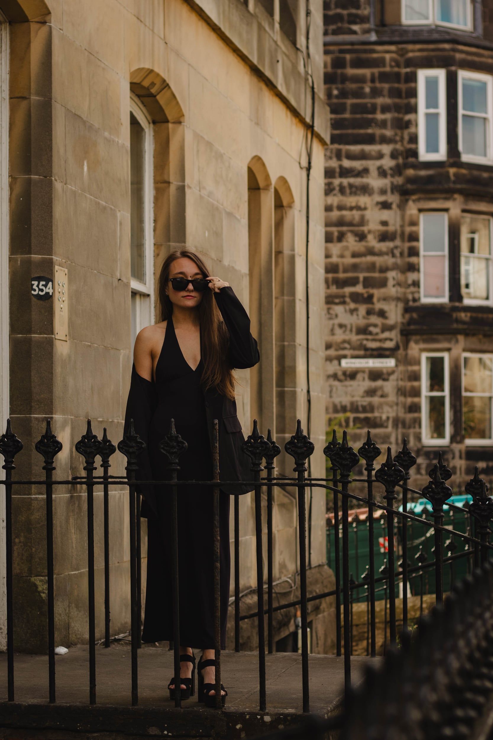 Woman in black standing by iron railings in front of a stone tenement
