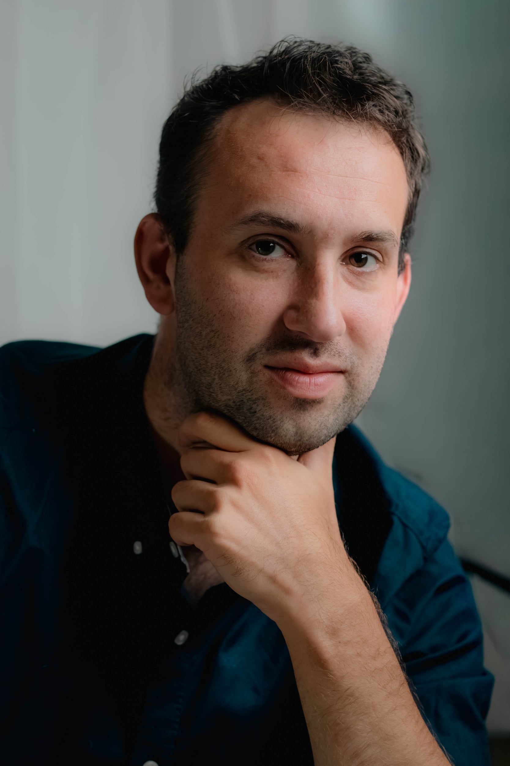 Man in a dark blue shirt, hand on chin