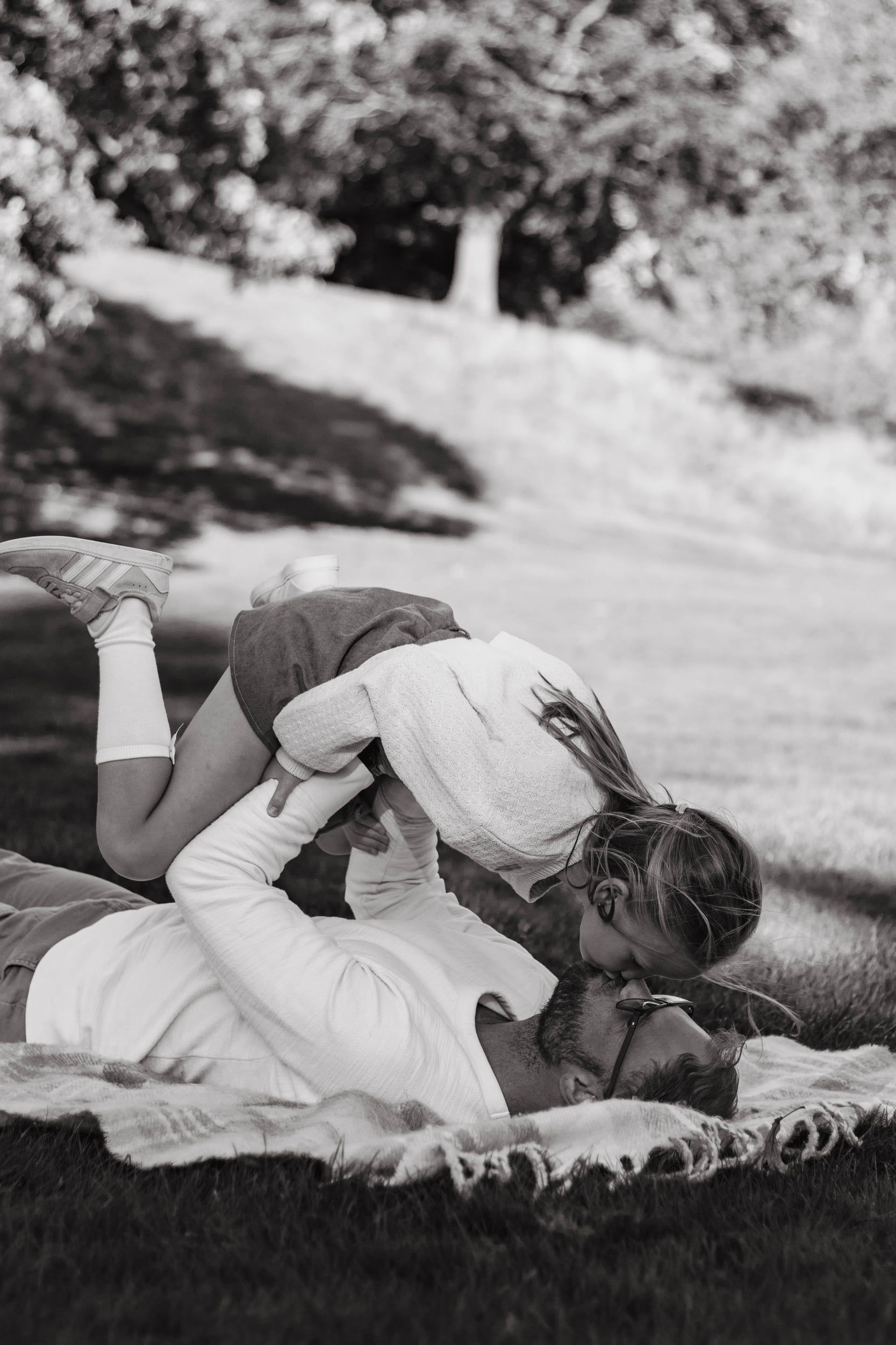 Black and white of a father lying on a blanket, lifting his daughter above him