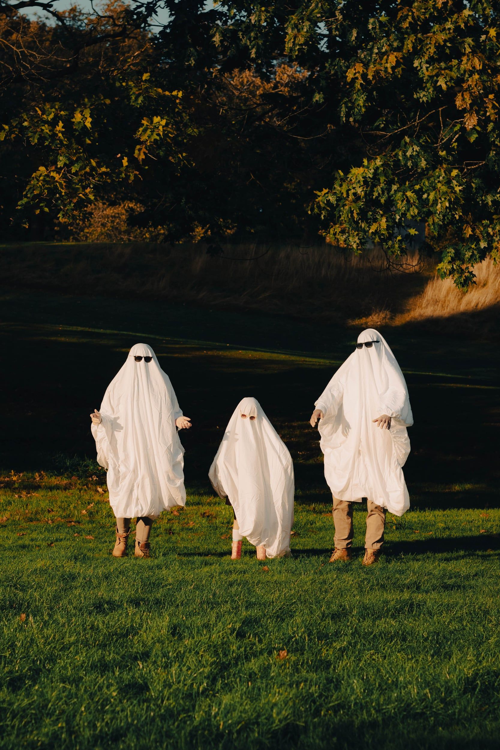 Three bedsheet ghosts in sunglasses standing in a park