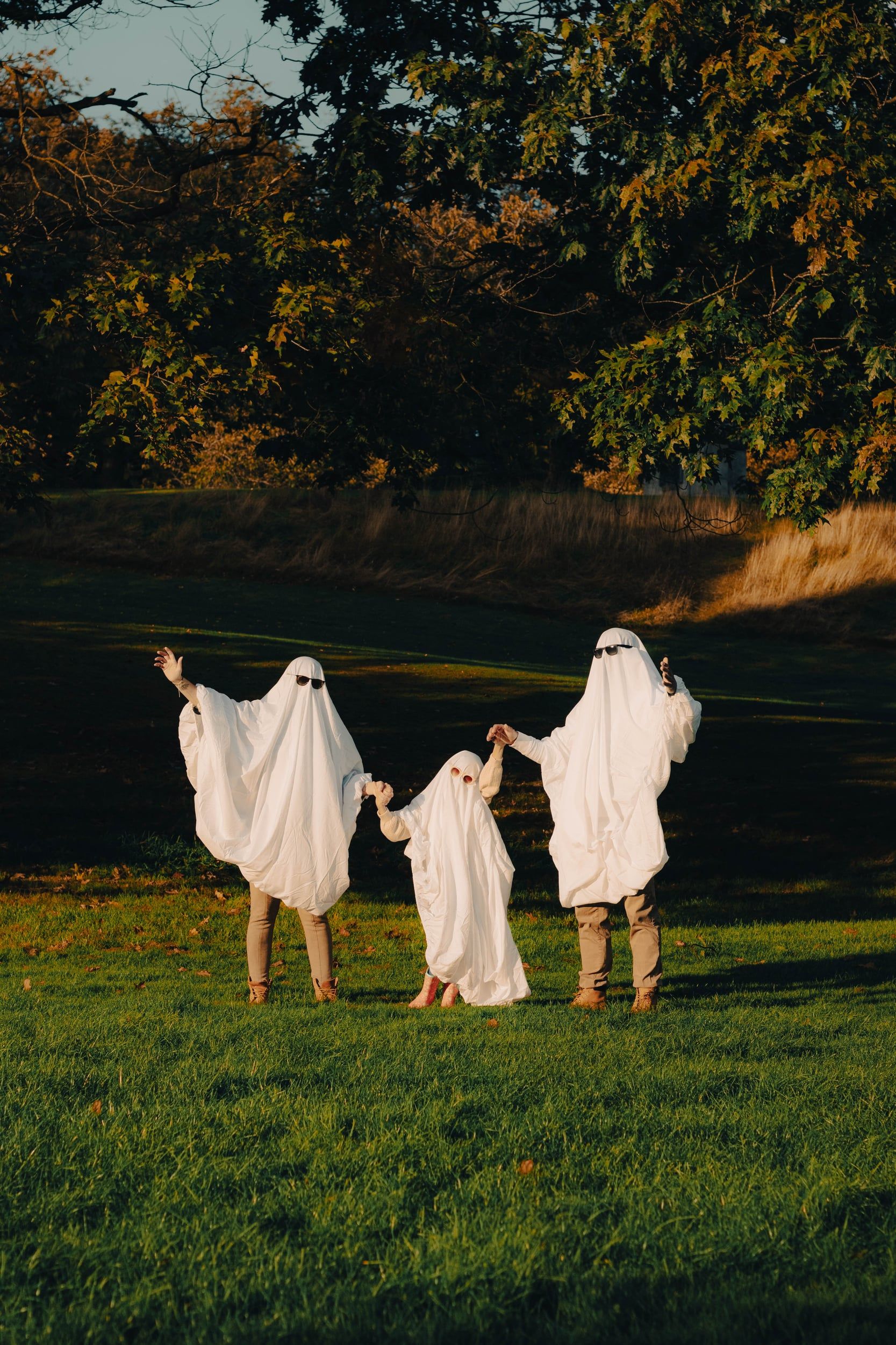 Family dressed as bedsheet ghosts waving on the grass in evening light