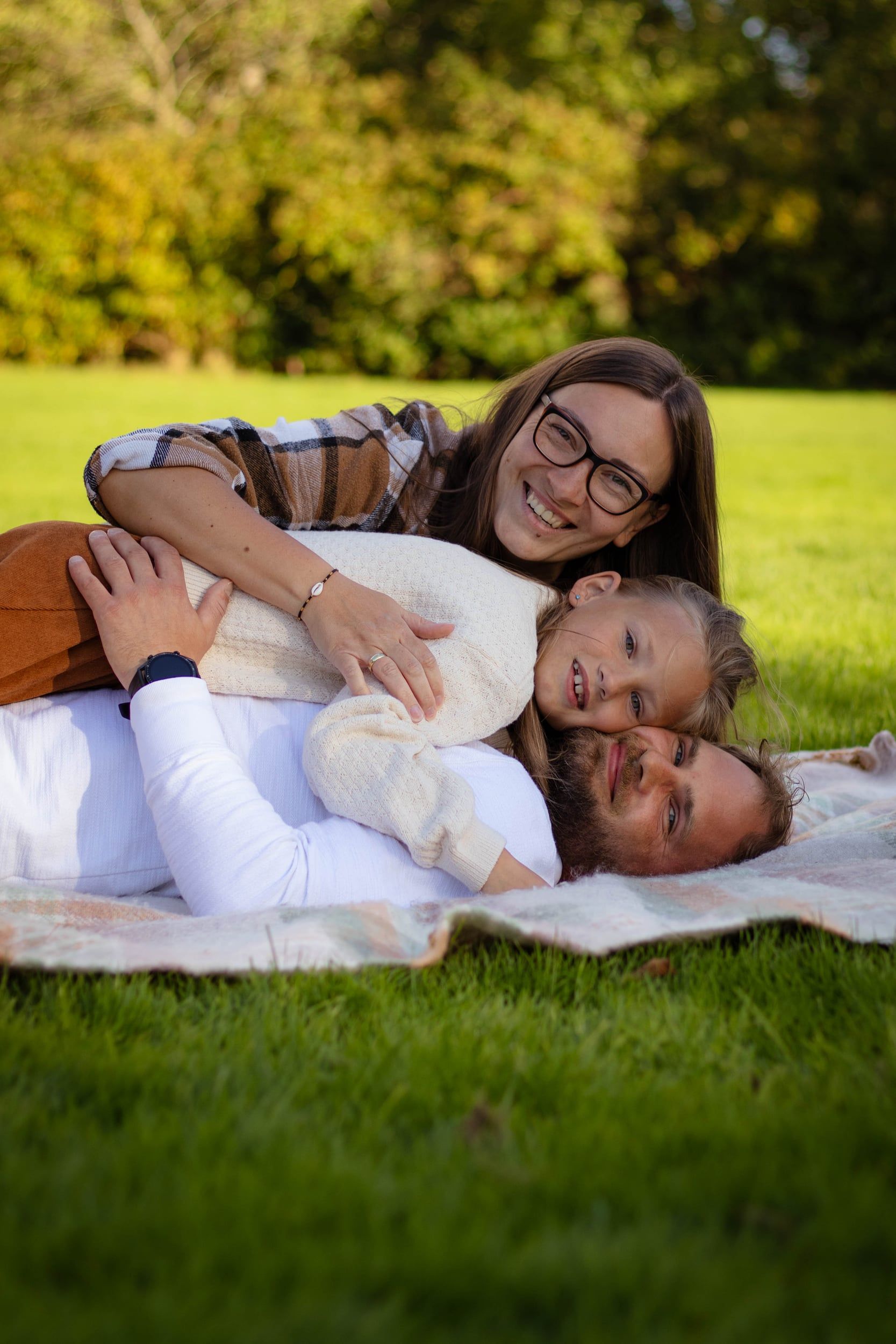 Mother, daughter and father piled up laughing on a blanket in the park