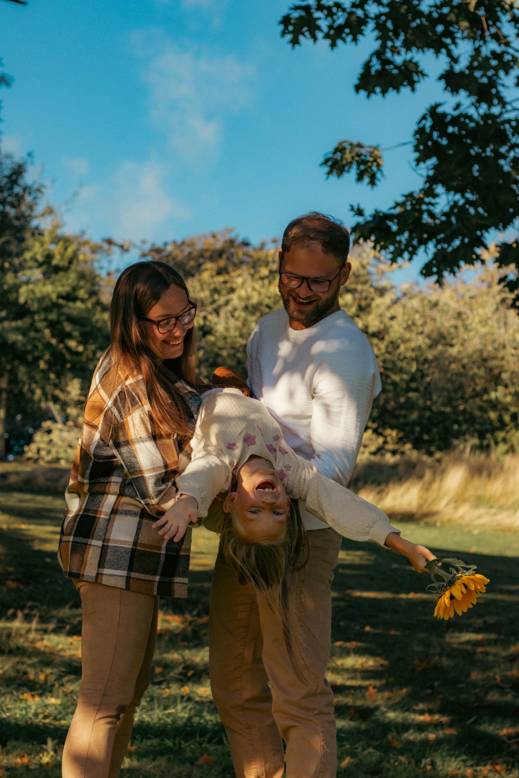 Parents swinging their laughing daughter upside down in an autumn park