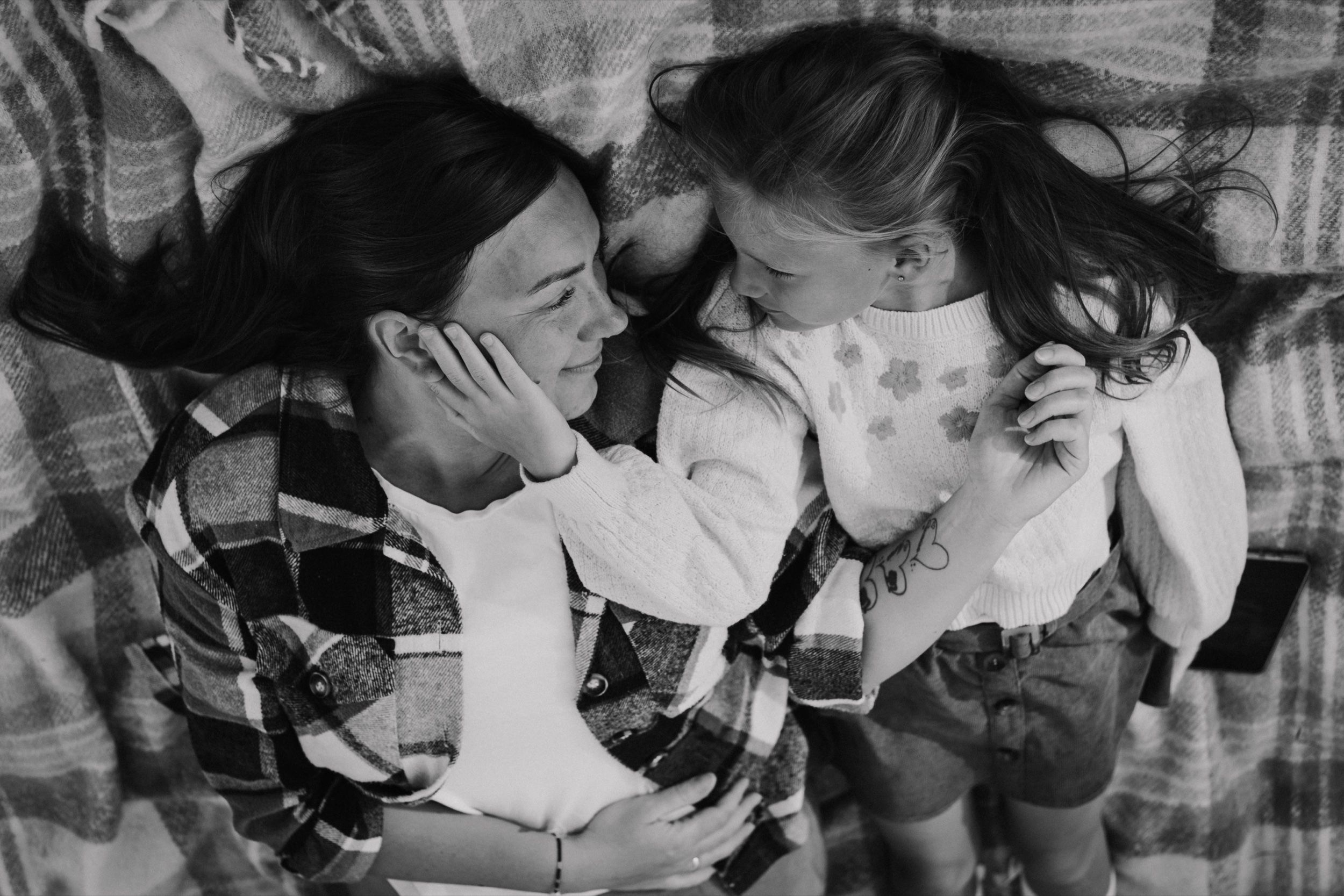 Black and white of a mother and daughter lying on a tartan blanket, face to face