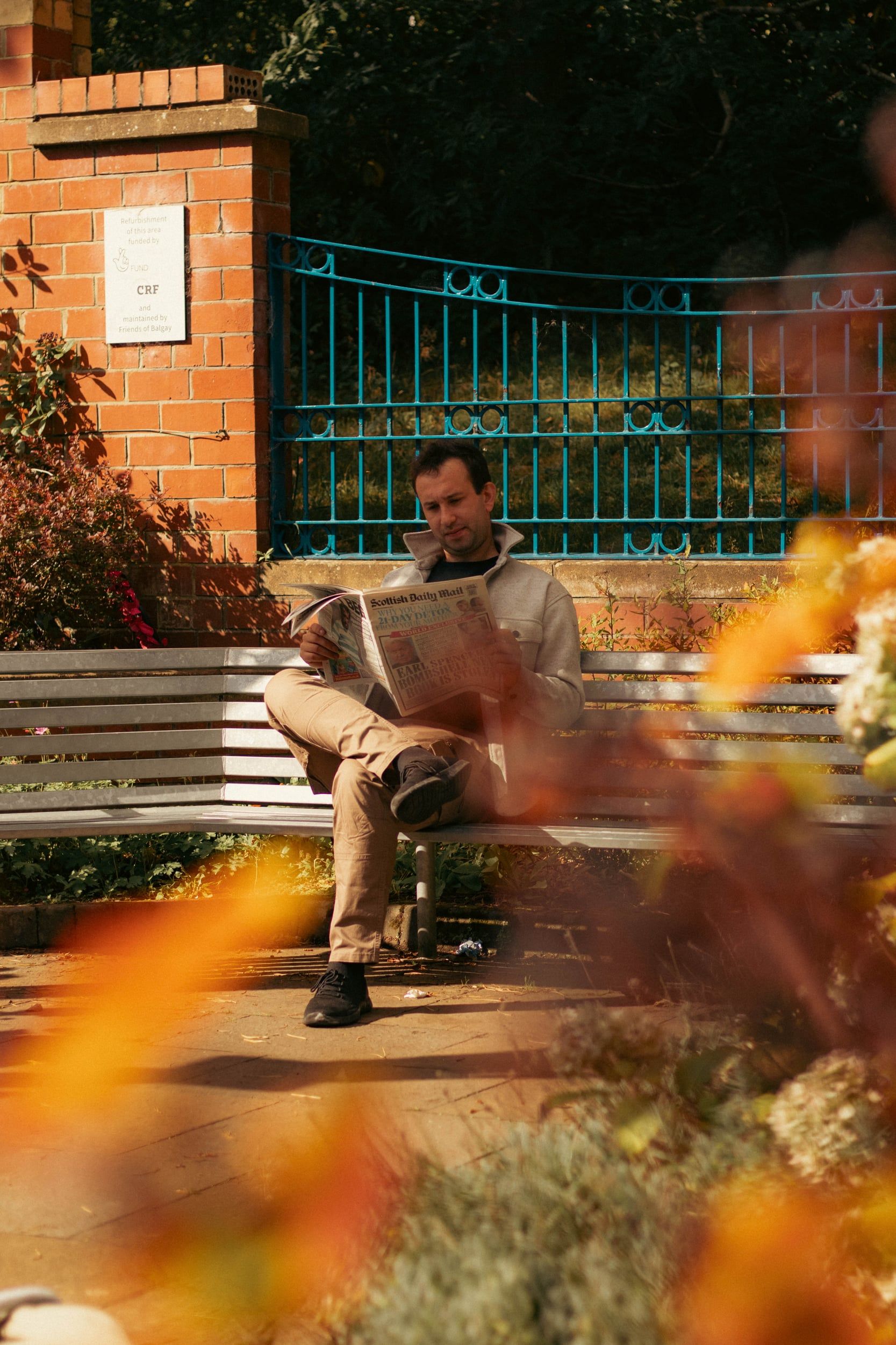 Man reading a newspaper on a park bench, autumn leaves in front
