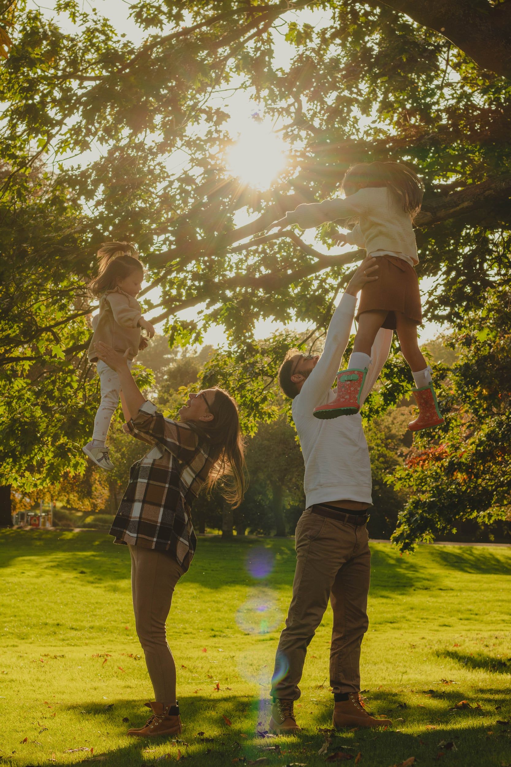 Parents lifting their two children high under a sunlit tree